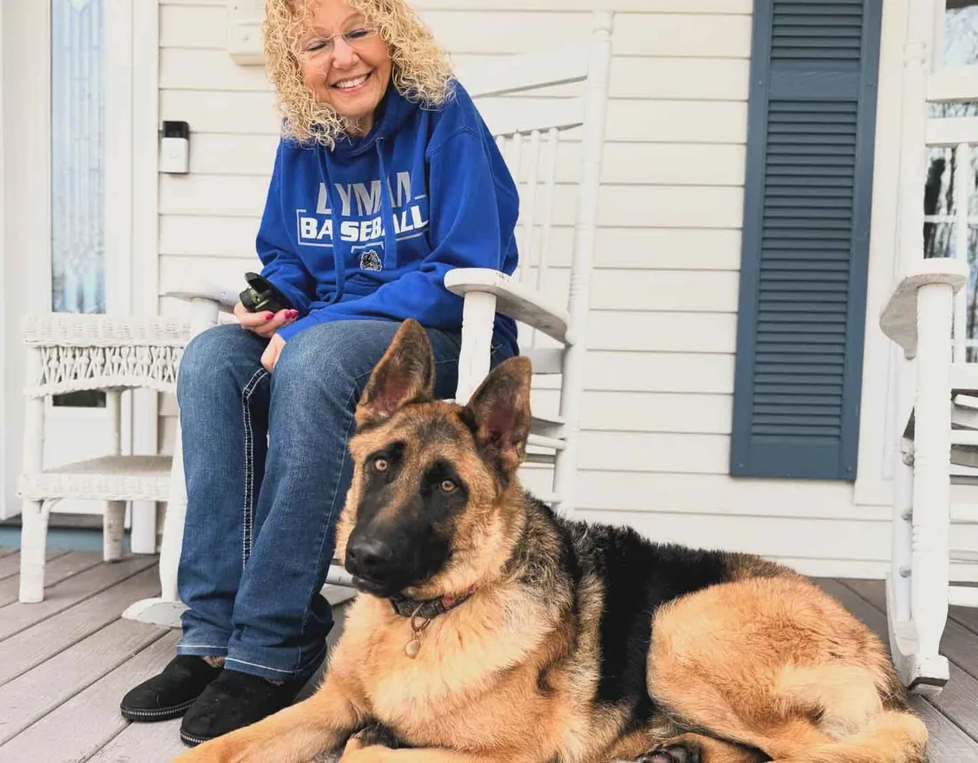 A dog owner relaxing on her front porch with her German Shepherd lying calmly beside her